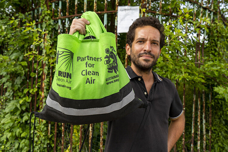 man holding green "partners for clean air" bag next to fence