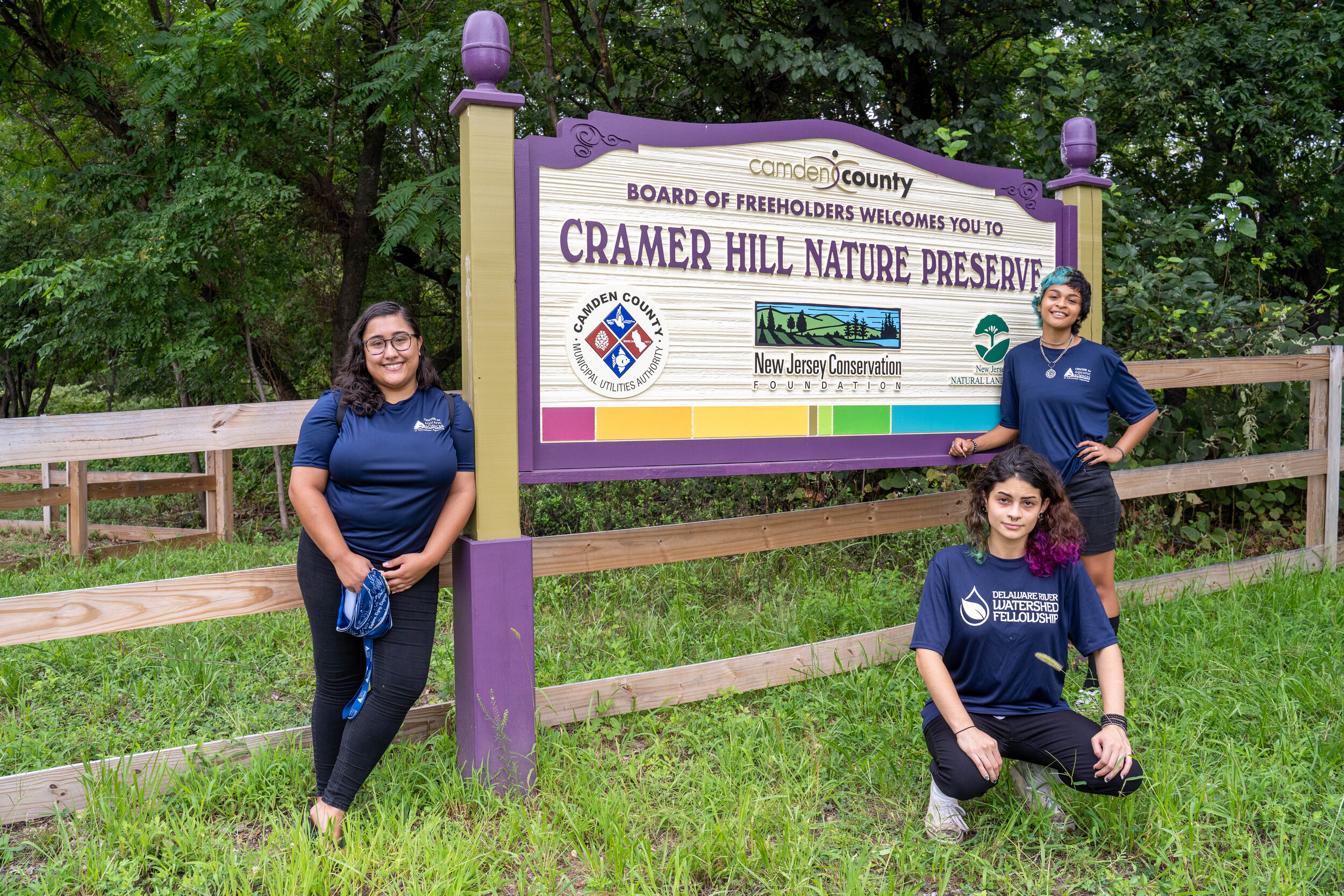 Three people posing in front of Cramer Hill Nature Preserve sign