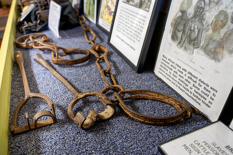 The Lest We Forget Slavery Museum displays signs used to segregate establishments and bathrooms based on race. Below: A case holds ironware used to restrain slaves. | Photography by Milton Lindsay