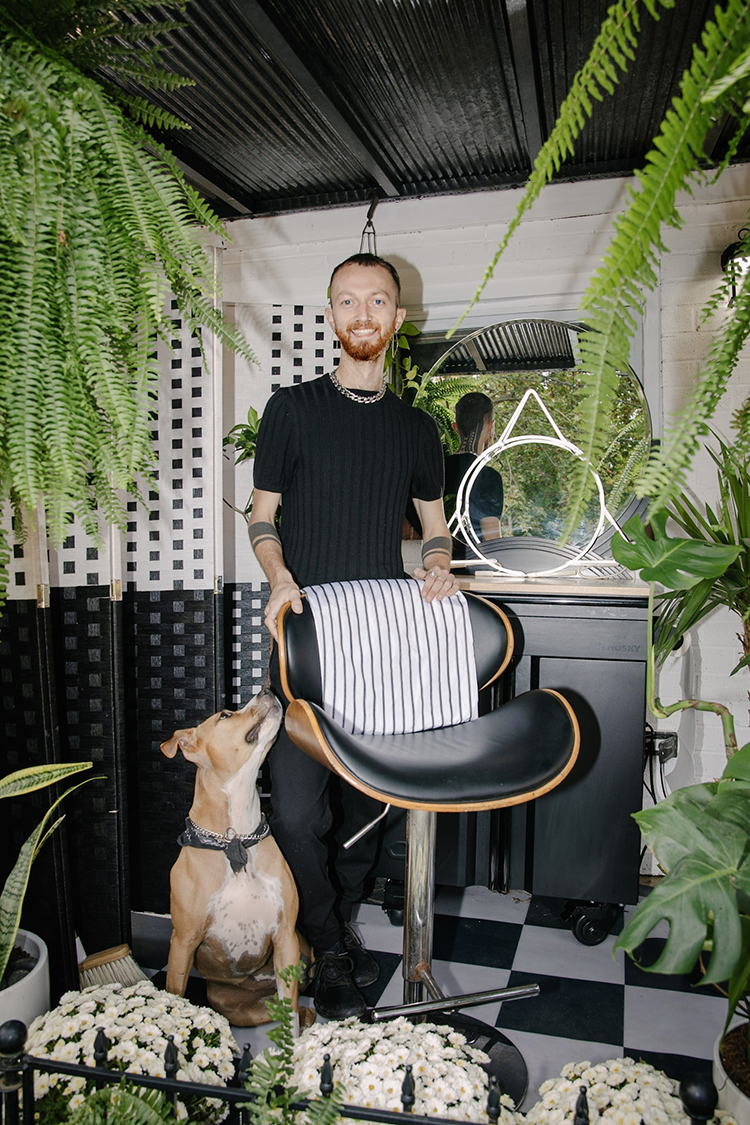 A person stands behind a barber's chair with dog