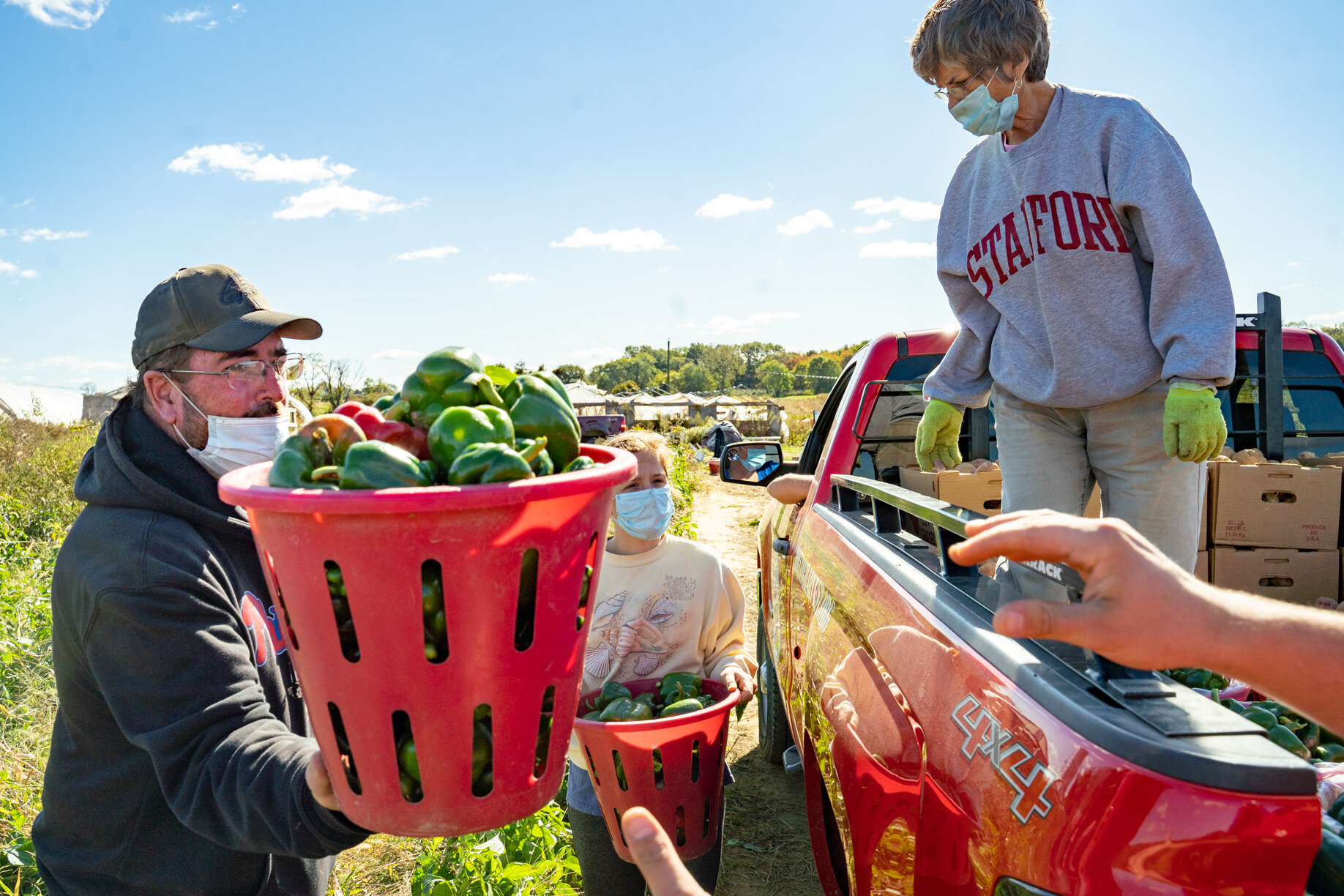 Bob Solly of Solly Brothers Farm in Warminster, Pennsylvania, hands a basket of gleaned peppers to Rolling Harvest volunteers. Volunteer JanWalters organizes the produce to fit neatly in the bed of the truck.Photography by Milton Lindsay.