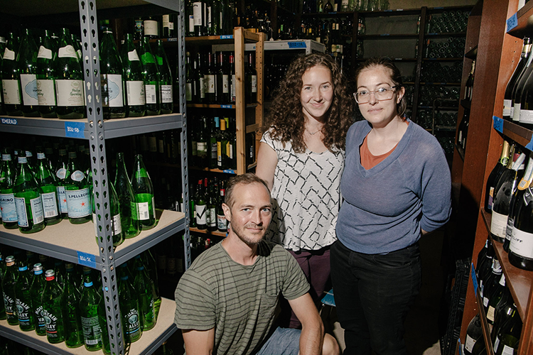 three people surrounded by shelves of bottles